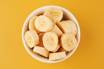 White cup with sliced bananas on a yellow background. Tropical fruits, healthy food, vitamins