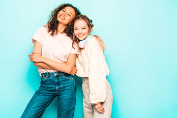 Two young beautiful smiling international hipster female in trendy summer clothes. Sexy carefree women posing near blue wall in studio. Positive models having fun. Concept of friendship