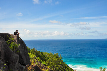 One tourist man sitting on a rock on the top of the hill in the viewpoint with the Indian ocean in...