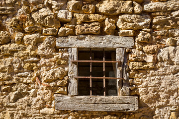 an old small wooden window with metallic protection bars on a stone wall