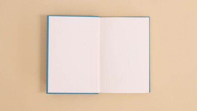Blue hardcover vintage book appear and open with copy space on beige background. Stop motion flat lay