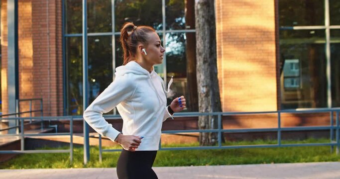 Side view of strong Caucasian woman in sportswear training, working out and running. Young female athlete doing sports to keep fit in morning in city street. Health, hard work concept.
