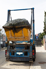 Camión cargando un contenedor con restos de poda.