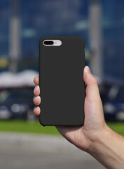 Black phone case mockup, smart phone on a blurry city background back view in man's hand