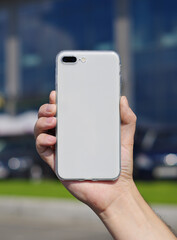 Smart phone on a blurry city background. in a white plastic case back view. Smart phone in man's hand. Template of phone case