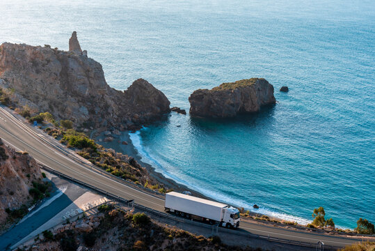 Truck with refrigerated semi-trailer driving on a road next to a beach.