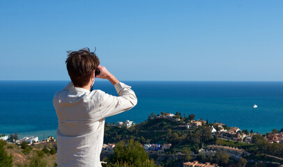 A closeup of an adventurous young explorer looking through binoculars over the town by the sea