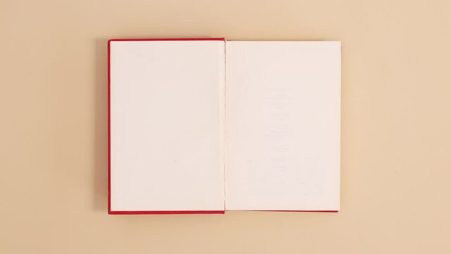 Red hardcover vintage book appear and open with copy space on beige background. Stop motion flat lay