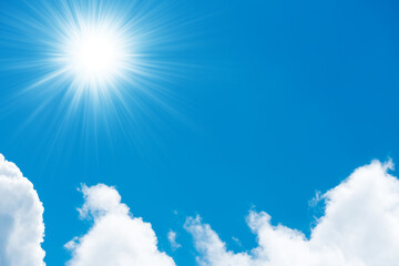 Beautiful fluffy white clouds on bright blue sky and shining sun with sun rays