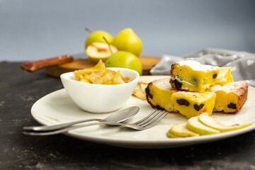 Sliced pie on a white plate with pear jam on a black table. Green pears in the background are blurred. Morning breakfast