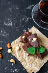 Homemade chocolate fudge garnished with mint leaves and served with tea on a black background. Nuts in the background blurred background. Copy space.