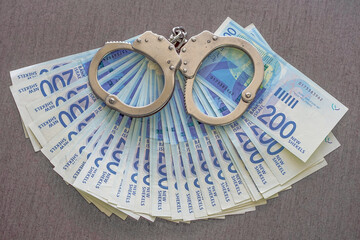 Handcuffs on the background of Israeli money. Police handcuffs. Financial crime, dirty money and...