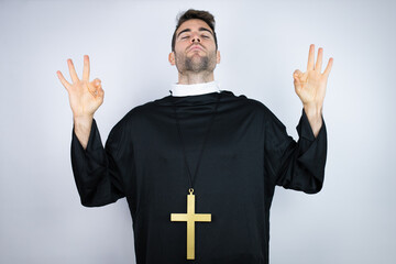 Young hispanic man wearing priest uniform standing over white background relax and smiling with...