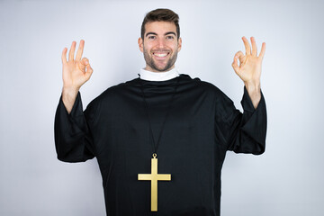 Young hispanic man wearing priest uniform standing over white background doing ok sign with fingers...