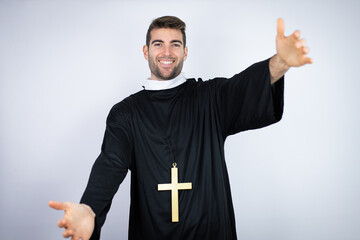Young hispanic man wearing priest uniform standing over white background looking at the camera...