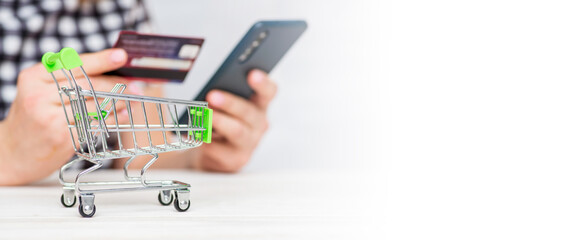 Shopping Cart and woman holding credit card and smartphone shopping online. Woman purchases goods from internet. Female makes payment on bank website