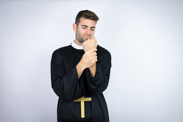 Young hispanic man wearing priest uniform standing over white background suffering pain on hands...