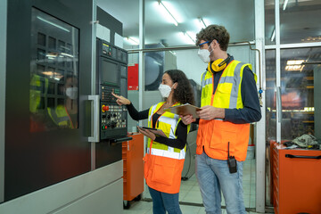 Two engineers wearing protection face mask working in control room machine in a large industrial factory.