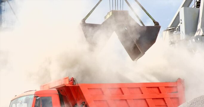 Grapple crane unloading cement clinker from ship to truck in port. Grab is discharging bulk cargo from a hold of cargo ship, causing dust in atmosphere. Loading in Harbor outdoors. Logistics