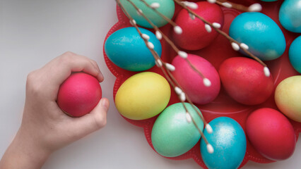 Hand with a painted egg on the background of a plate with colorful Easter eggs and a willow branch