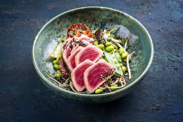Modern style traditional Japanese gourmet seared tuna fish steak tataki with soba noodles and stir-fried vegetables served as close-up on a Nordic design bowl with copy space