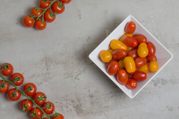 red and yellow small tomatoes in white square bowl. branches of red tomatoes are nearby. Flat lay 