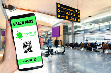 The digital green pass of the european union with the QR code on the screen of a mobile held by a hand with blurred airport in the background. Immunity from Covid-19. Travel without restrictions.