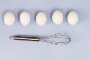 group of white chicken eggs on light blue background with stainless steel whisk , empty space for text
