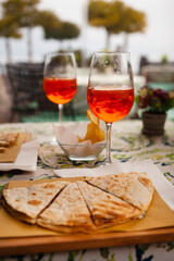 Italian traditional street food and aperitif. Aperol spritz with Piadina or Piada which is a thin Italian flatbread with cheese, ham, rocket, arugula, tomatoes in the northern Italy, Lombardy, Milan.