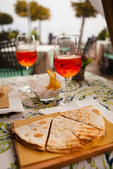 Italian traditional street food and aperitif. Aperol spritz with Piadina or Piada which is a thin Italian flatbread with cheese, ham, rocket, arugula, tomatoes in the northern Italy, Lombardy, Milan.