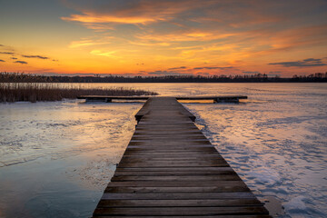 Fototapeta na wymiar beautiful, fabulous sunset over the frozen lake and the pier - Lake Rotcze