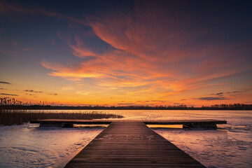 Obraz na płótnie Canvas beautiful, fabulous sunset over the frozen lake and the pier - Lake Rotcze