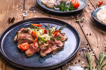 Beef tenderloin fried on fire with herbs, seasoned with spices, tomatoes. Wooden brown background decorated with rosemary, spices.