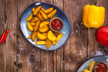 Fried potatoes with sauce on a plate on a brown wooden background, decorated with Bulgarian pepper, coarse salt, spices.