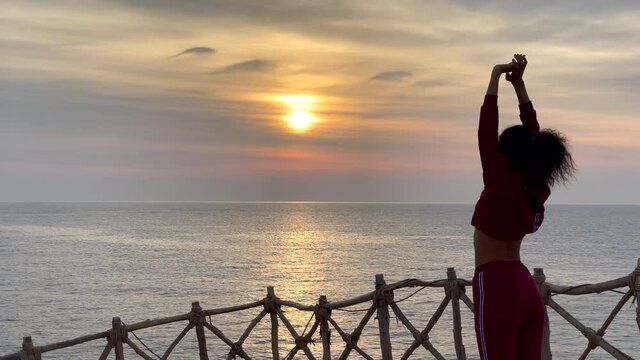 Stress relief. Young woman admiring sea view while doing breathing exercises at sunrise. Slow motion. Copy space on the left side. Body positive, healthy lifestyle, nature concept