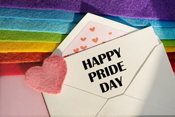 An open envelope with the text HEPPY PRIDE DAY, on a pink and blue background with a decor of felt hearts and a flower. Flat lay, top view. LGBT concept.