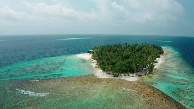 A scenic aerial view of a drone flying over a calm ocean with a coral reef to a tropical island paradise.. Thinadhoo (Vaavu Atoll), Maldives