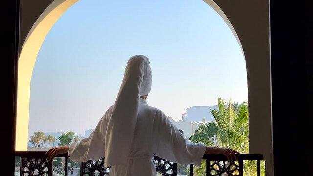 Best view. Rear view of young woman in bathrobe admiring the view from the hotel balcony on vacation. Luxury resort, relax, leisure activity concept