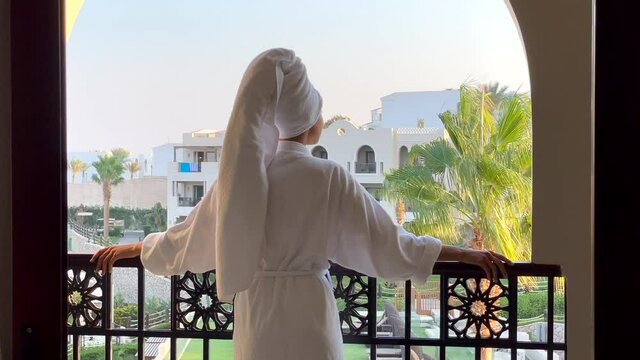 Feel the class. Rear view of young woman in bathrobe admiring the view from the hotel balcony on vacation. Summertime, relax, leisure activity concept