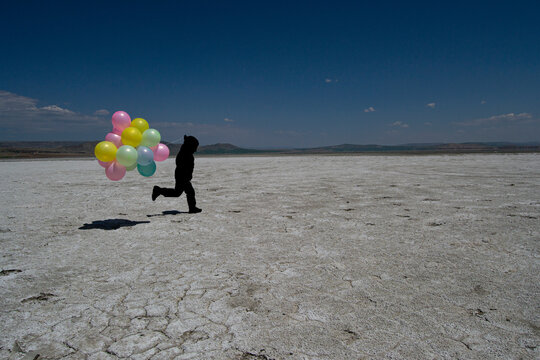 Silhouette Of A Boy Running In The Sand With Colorful Balloons In His Hand