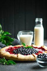Homemade galette with blueberries and plums with milk on a dark background.