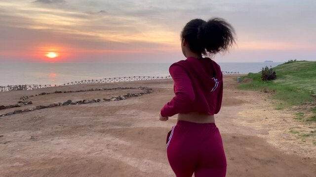 Notice the beauty around you. Active young woman running to the edge of the cliff at sunrise. Slow motion. Body positive, healthy lifestyle, nature concept. Rear view
