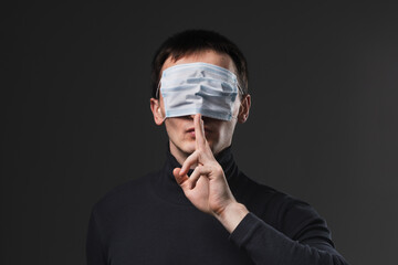 Man with medical mask on his eyes showing secret finger gesture. Concept of anti vaxxer and...