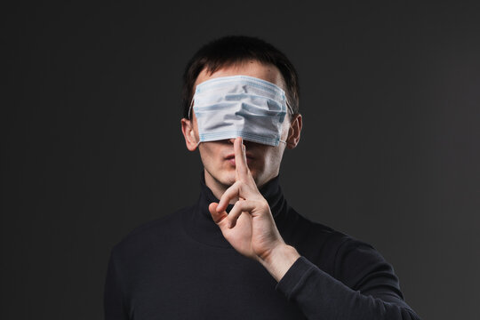 Man with medical mask on his eyes showing secret finger gesture. Concept of anti vaxxer and disinformation during global virus pandemic.