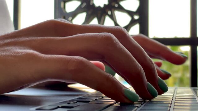Remote job. Close up of female hands typing on keyboard while working on the laptop, sitting on the terrace. Freelance, telework, summertime concept. Slow motion