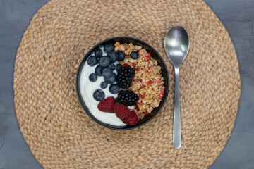 Muesli with yougurt and fresh berries in black bowl on dark gray background. Top view.