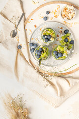 Healthy breakfast chia pudding with kiwi, blueberries and coconut slices, three portions in glass jars on a white table.
