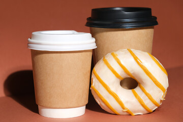 Coffee to go with glazed donut. Hot drinks paper containers and donut on brown background.
