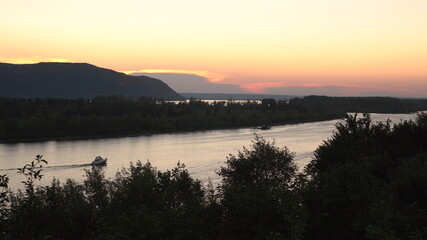 Naklejka premium View of the mountains and the river at sunset. View from a hill. Boats float on the river.