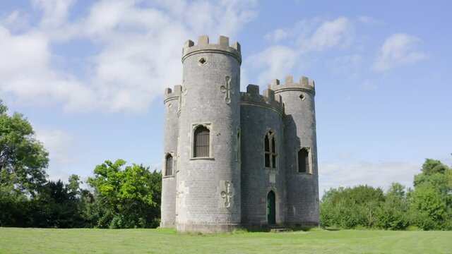 Low aerial around 18th century gothic British folly castle with three turrets on a sunny day with trees in the background. High quality 4k footageLow aerial around 18th century gothic British folly
